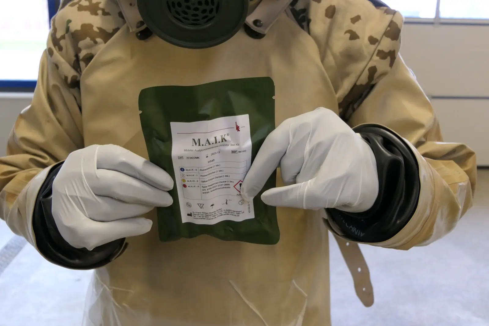 Person in Schutzkleidung hält ein MAIK Testkit hoch